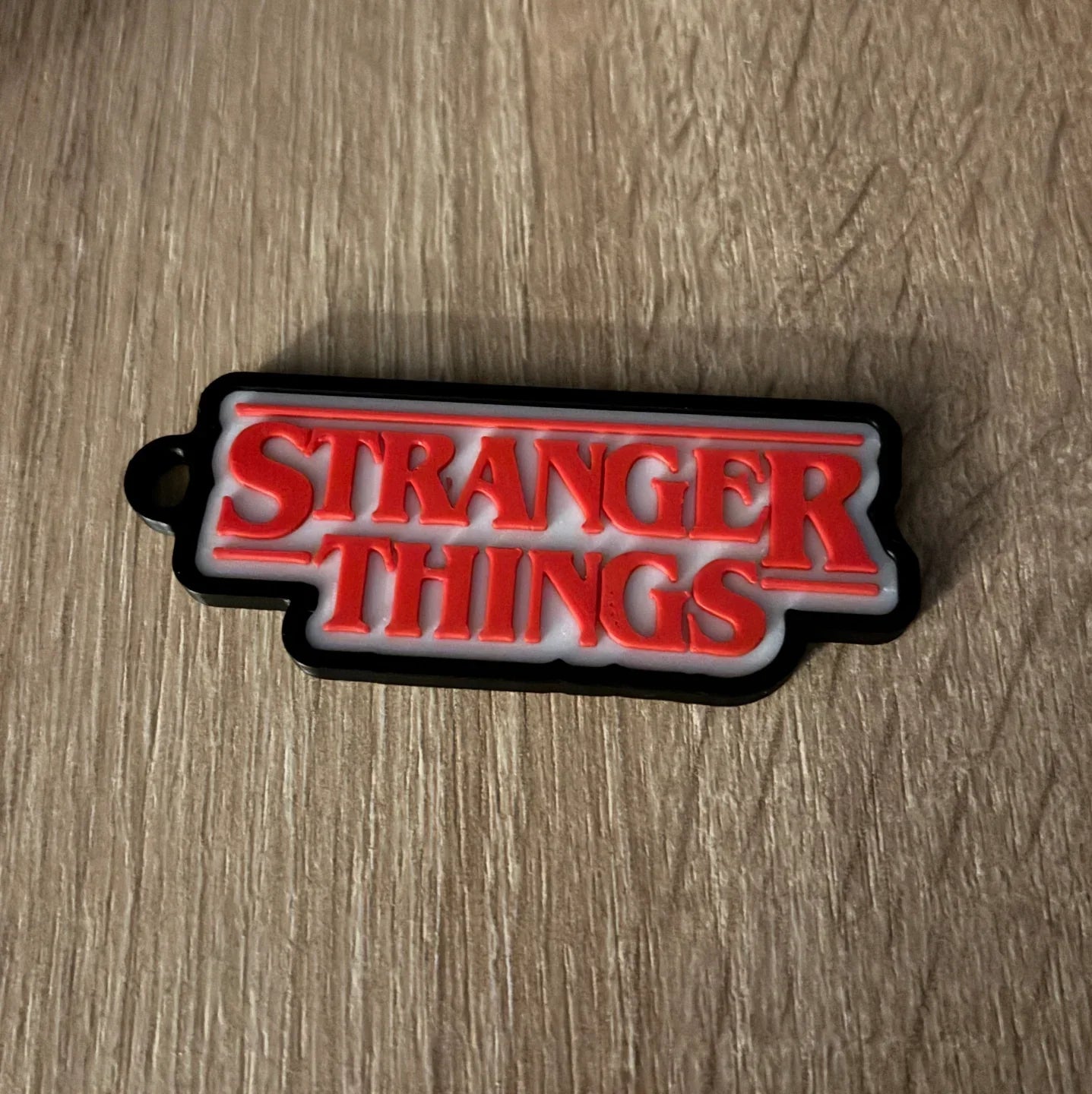 3D printed Stranger Things logo keychain on wood surface, modern Lunqo design