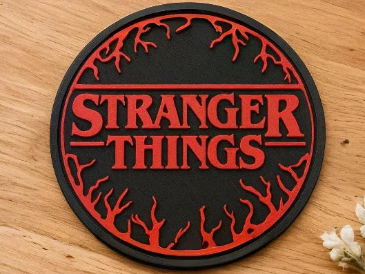 Round 3D printed Stranger Things coaster with red text and branch design on wooden table