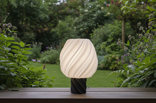 Modern 3D printed lamp with twisted design on a wooden table in a lush garden, Lunqo style