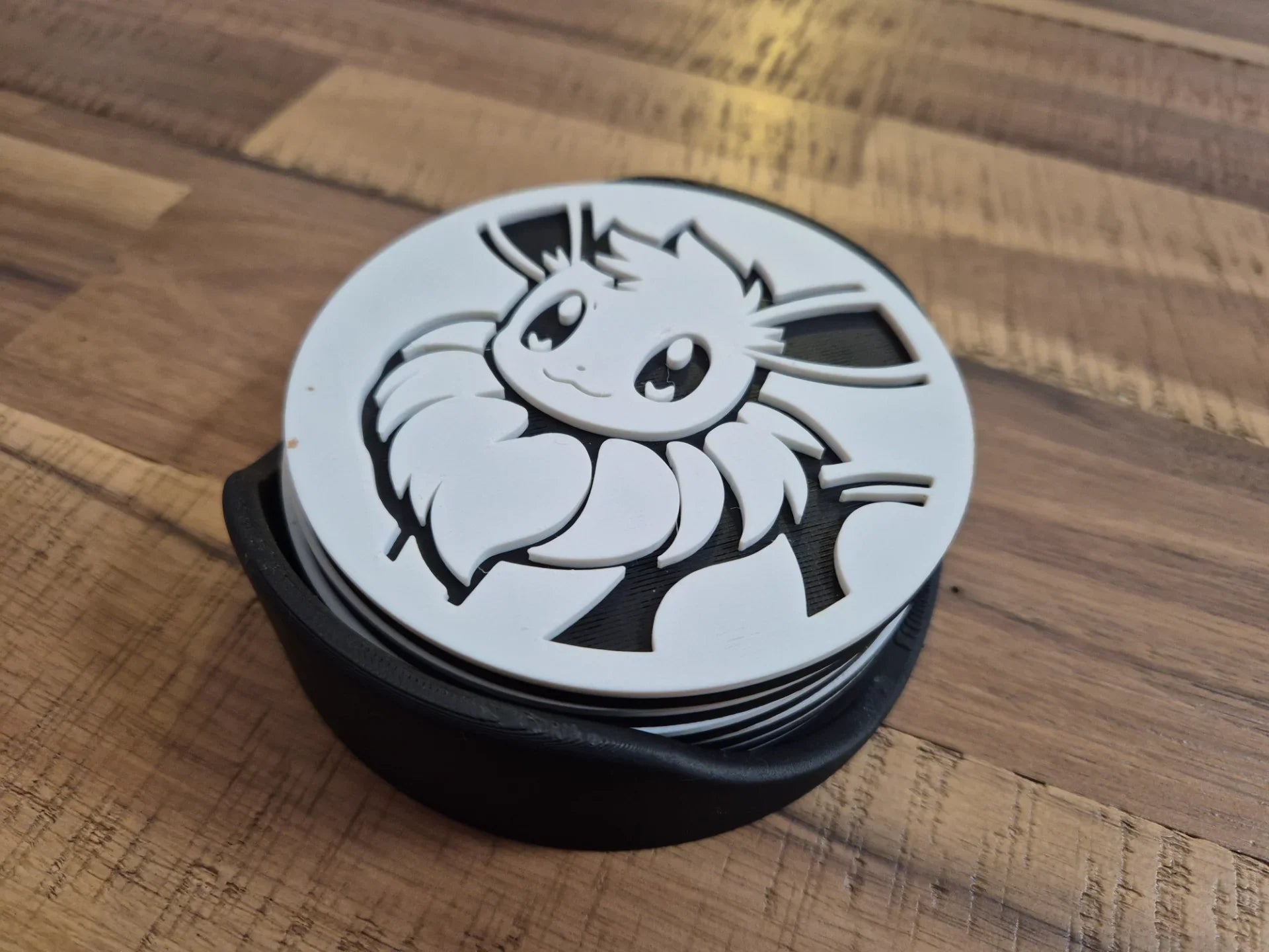 3D printed white and black coaster with cute animal design in a holder on wooden table