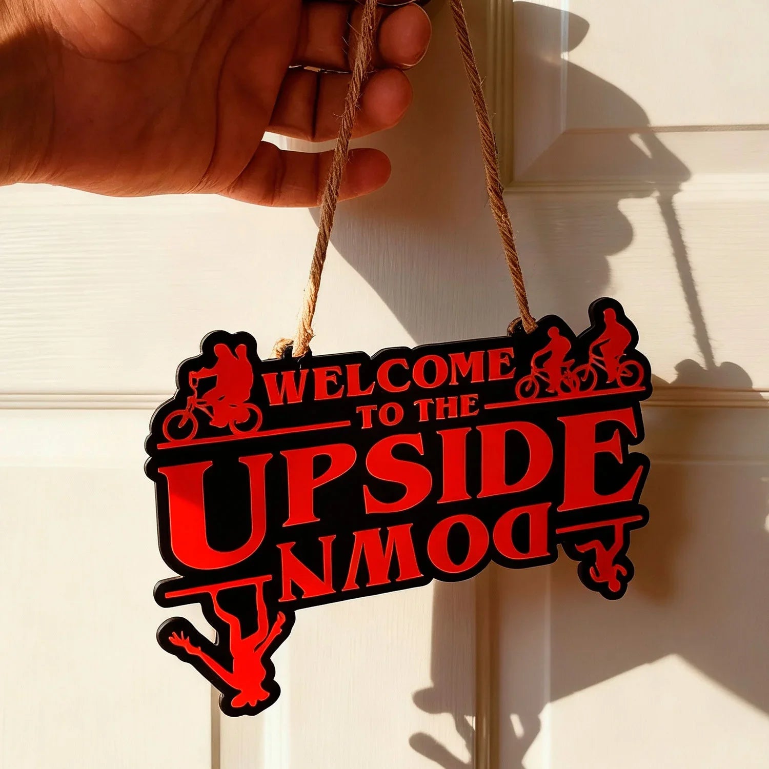 Hand holding Lunqo 3D printed sign reading 'Welcome to the Upside Down' with red text and bicycle silhouettes