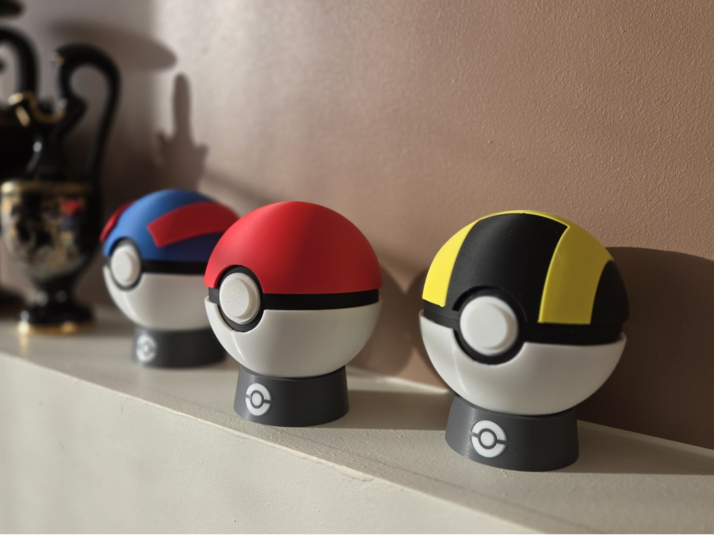 Three 3D printed Poké Ball designs in red, blue, and yellow on a shelf, modern Lunqo decor.