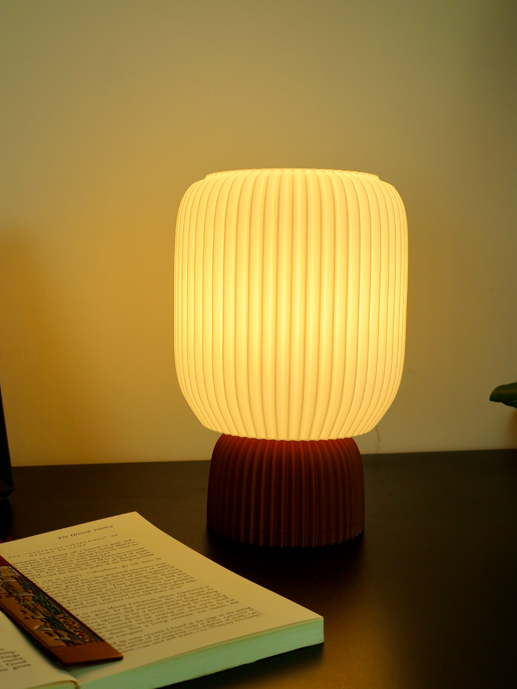 Modern 3D printed table lamp with ribbed design base, soft glow, on dark desk near open book