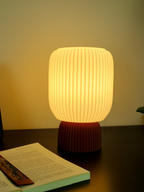 Modern 3D printed table lamp with ribbed design base, soft glow, on dark desk near open book