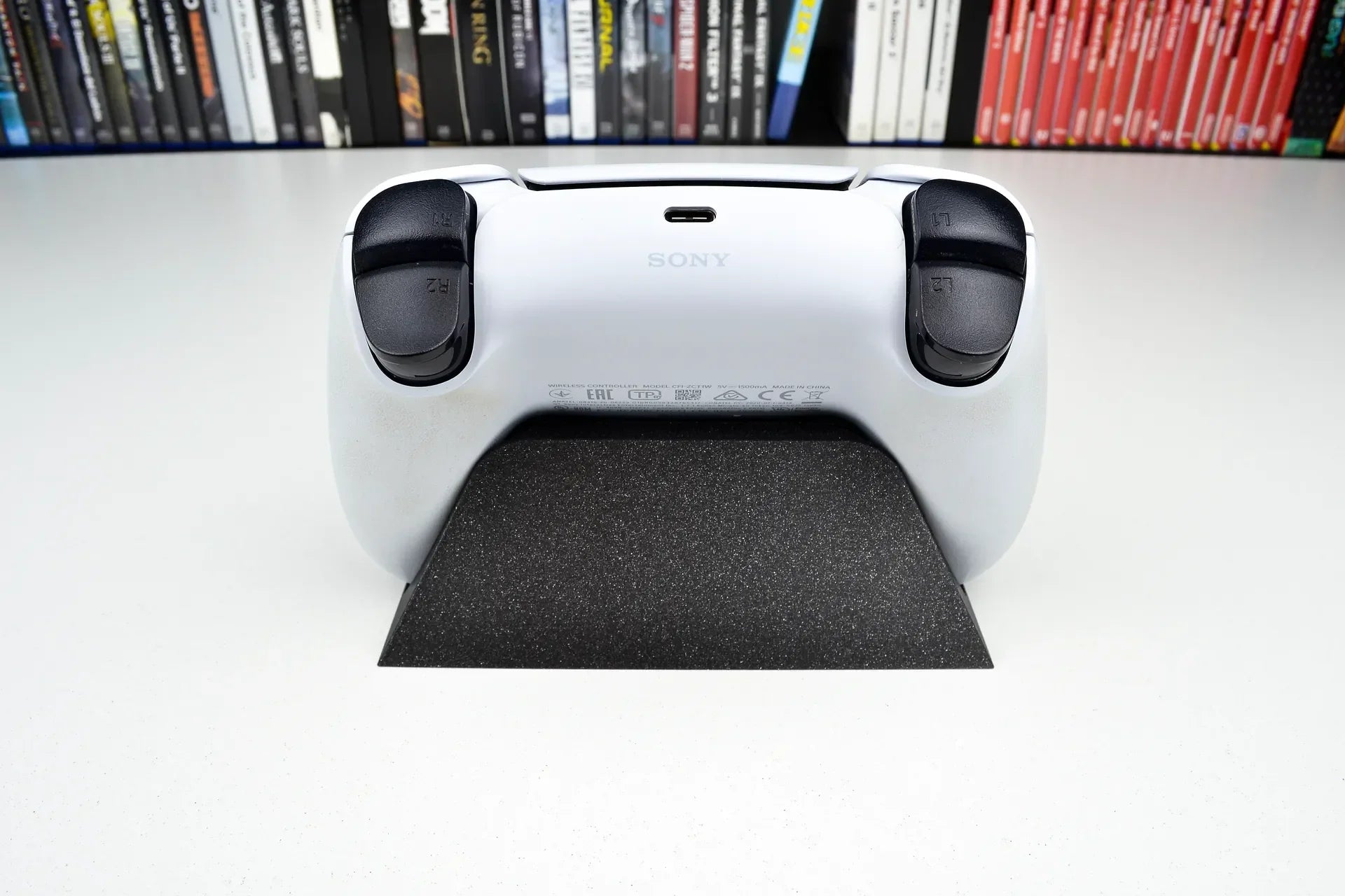3D printed minimalist stand holding a PlayStation controller, with game cases in background