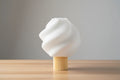 White ceramic sculpture on a wooden base against a gray background