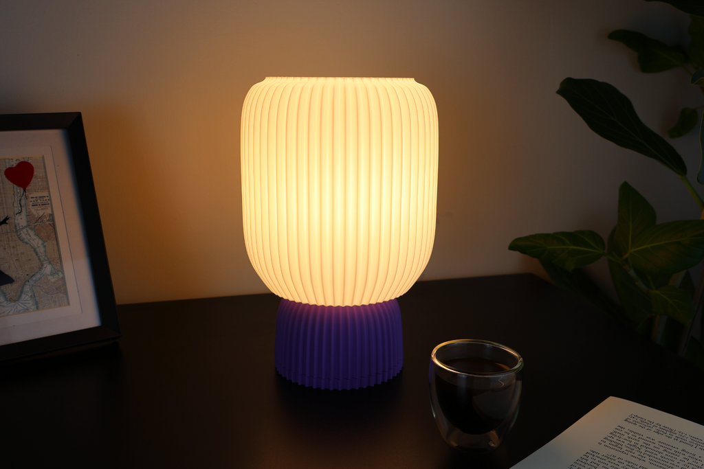 Modern 3D printed table lamp with ribbed shade, purple base, on desk with coffee and plant
