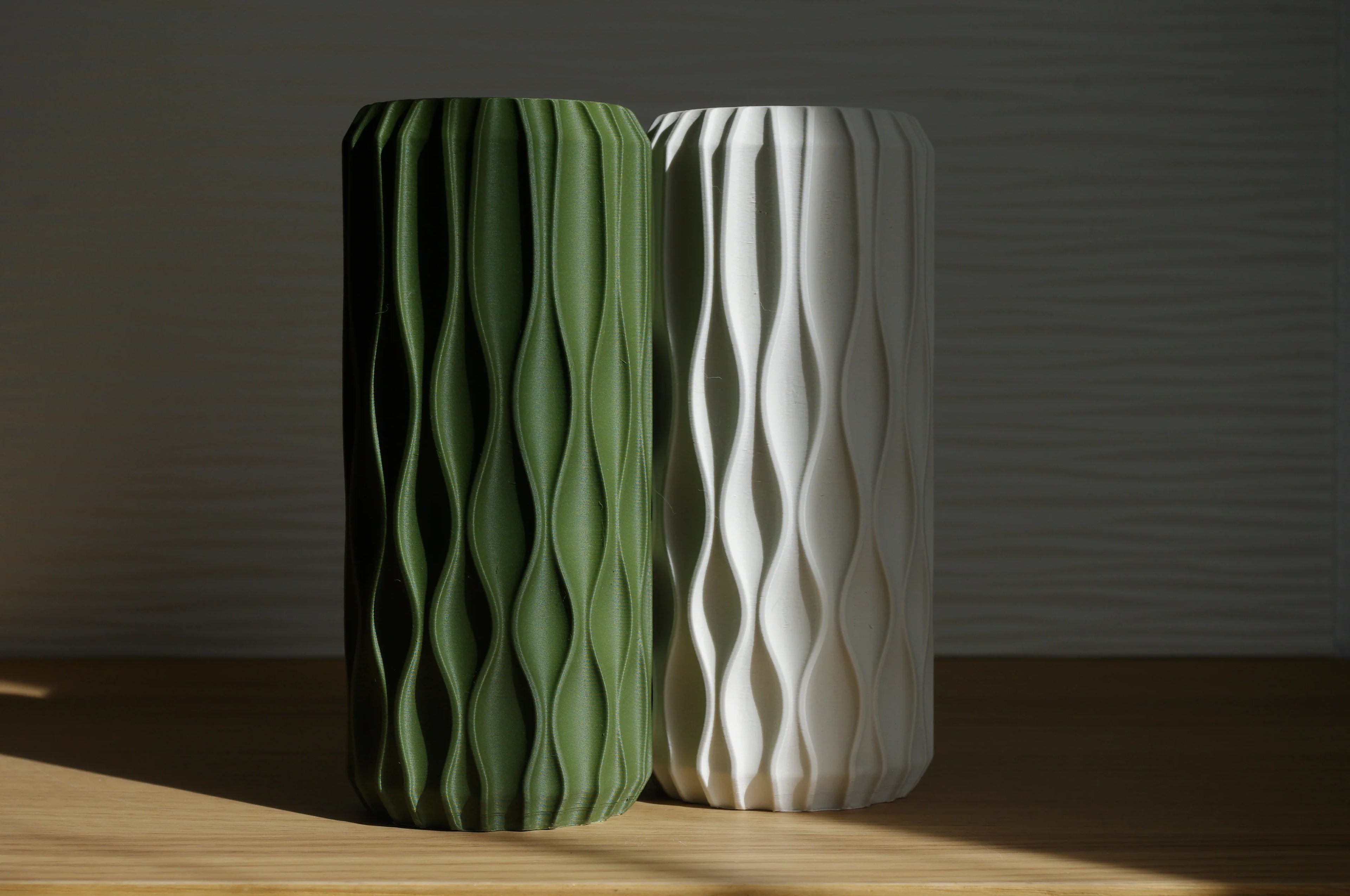 Two textured vases, one green and one white, on a wooden surface with a dark background.
