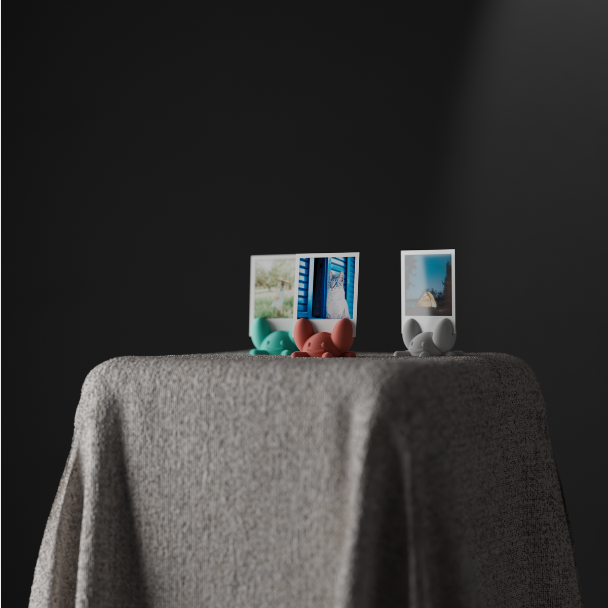 Three crab-shaped instant photo holders arranged on a dark draped pedestal
