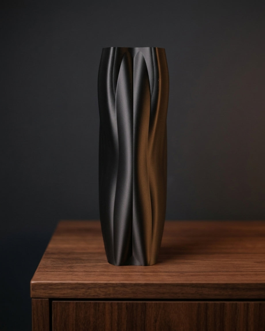 Tall black sculptural vase displayed on dark wood against a moody backdrop.