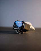 Black Mini Wibble Apple Watch charger stand holding a watch on a dark desk