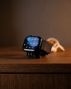 Black Mini Wibble Apple Watch charger stand in use on a bedside surface
