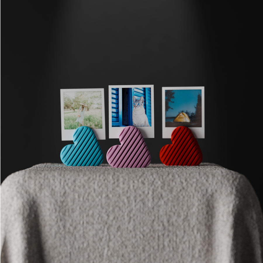 Three striped heart photo holders in blue, pink and red displaying small instant photos