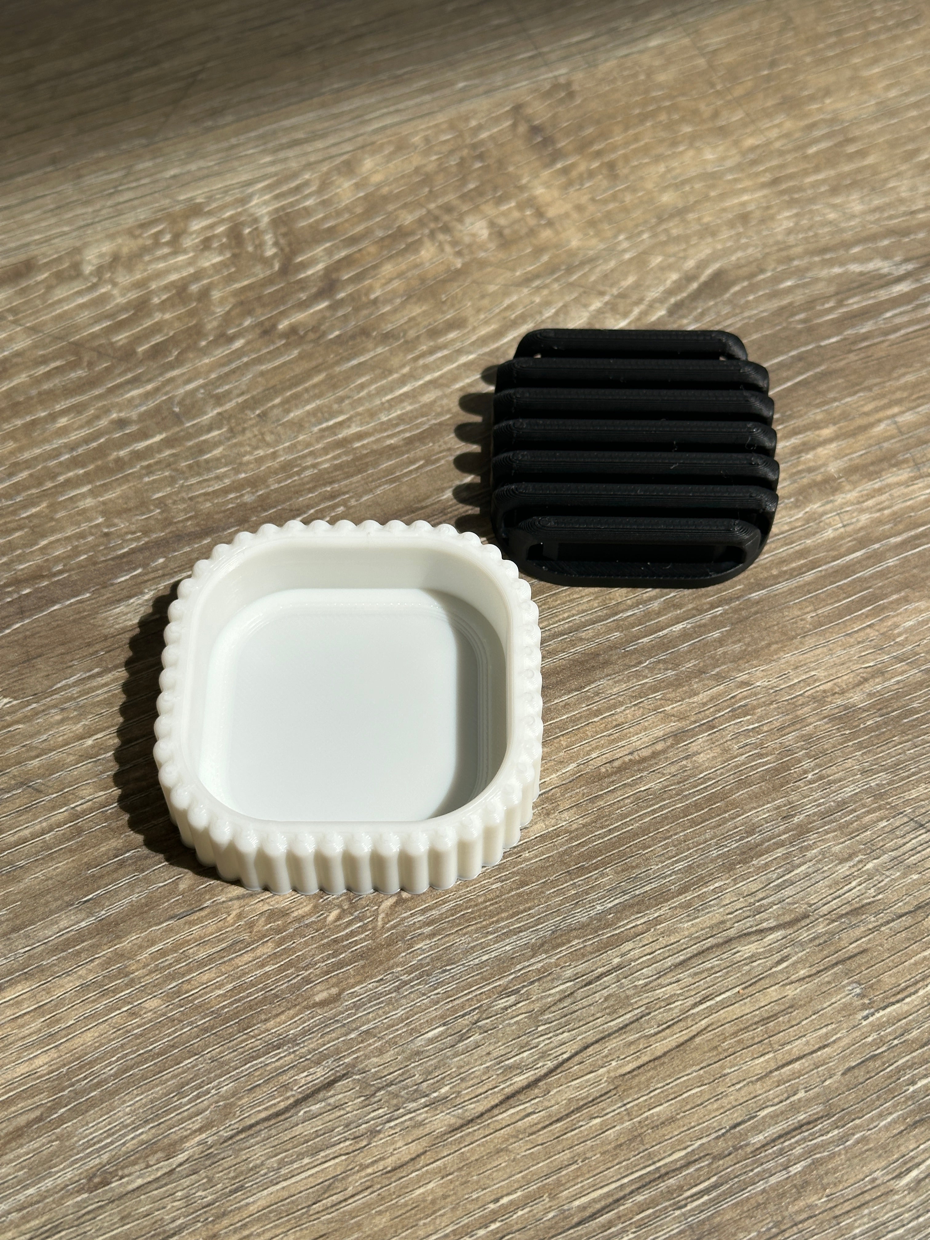 White outer stand and black removable drainage insert displayed separately on a wooden surface