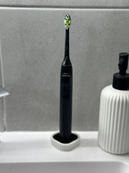 Black electric toothbrush standing upright in the white and black draining holder by a sink