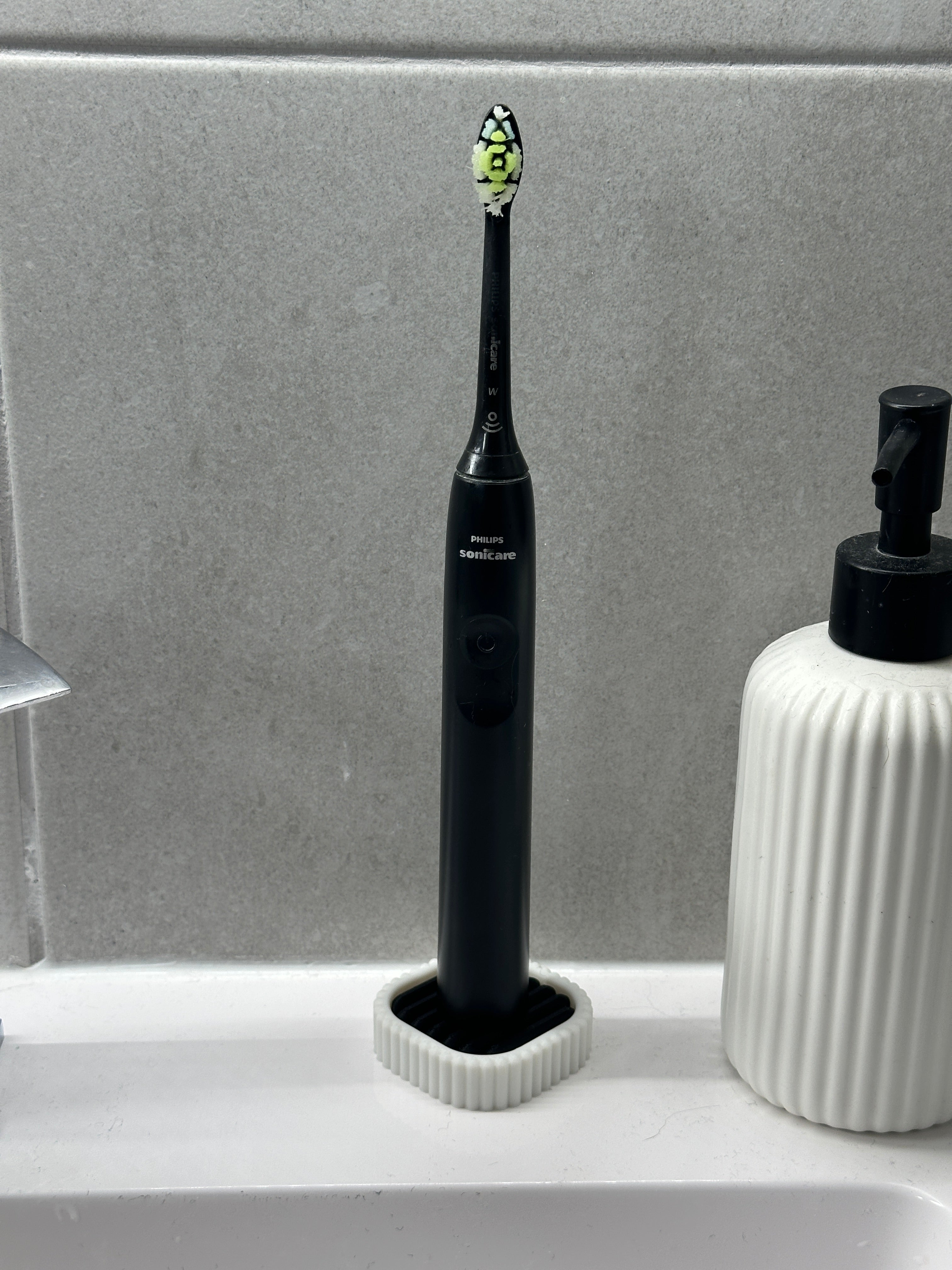 Black electric toothbrush standing upright in the white and black draining holder by a sink