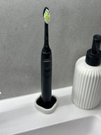 Electric toothbrush held upright in the compact white stand beside a ribbed soap dispenser