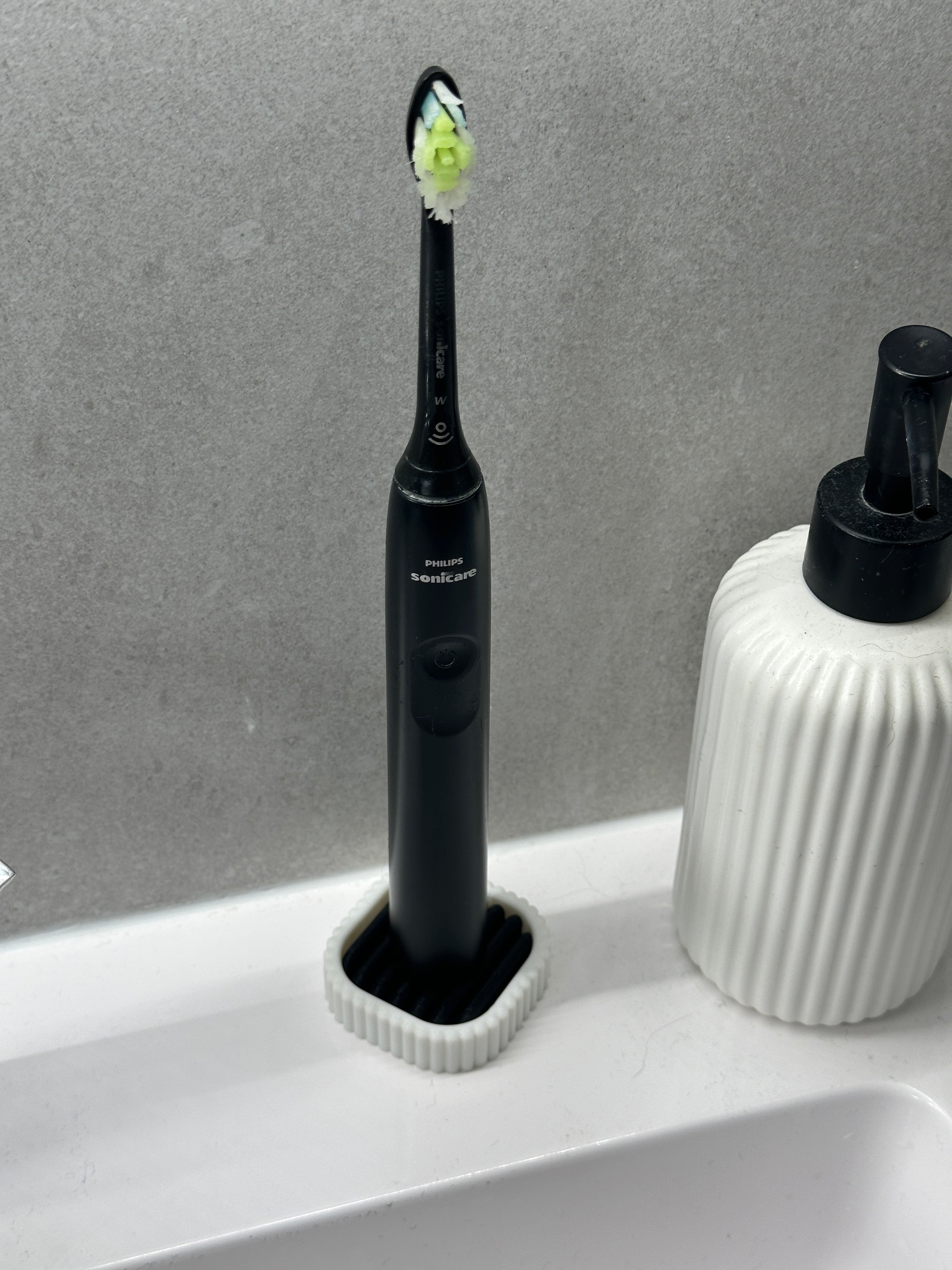 Electric toothbrush held upright in the compact white stand beside a ribbed soap dispenser