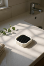 White electric toothbrush stand with black insert positioned near a sunlit bathroom basin