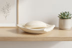 White rippled soap dish with a bar of soap styled on a wooden bathroom shelf.