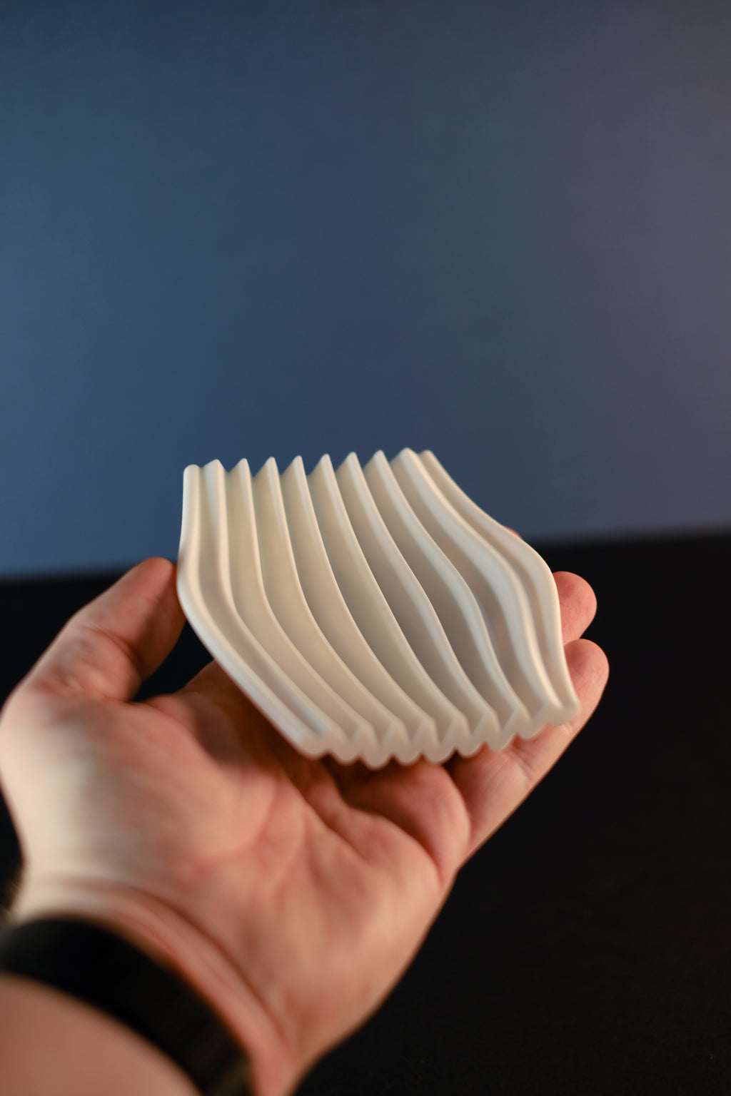 Hand holding the white Rippl soap dish to show its curved ripple channels.