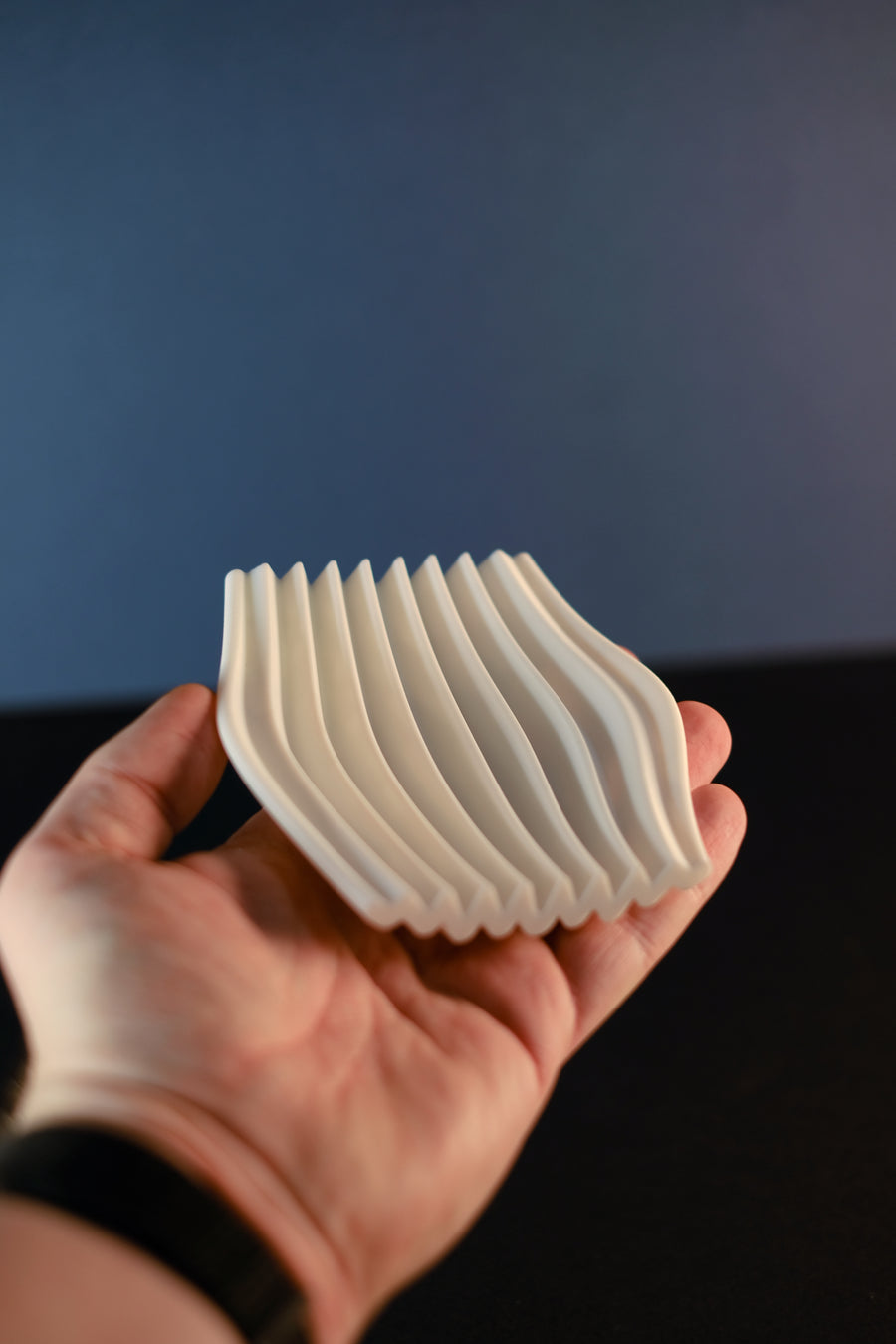 Hand holding the white Rippl soap dish to show its curved ripple channels.