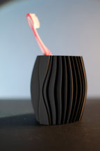 Close front view of the black ripple toothbrush holder with one pink toothbrush