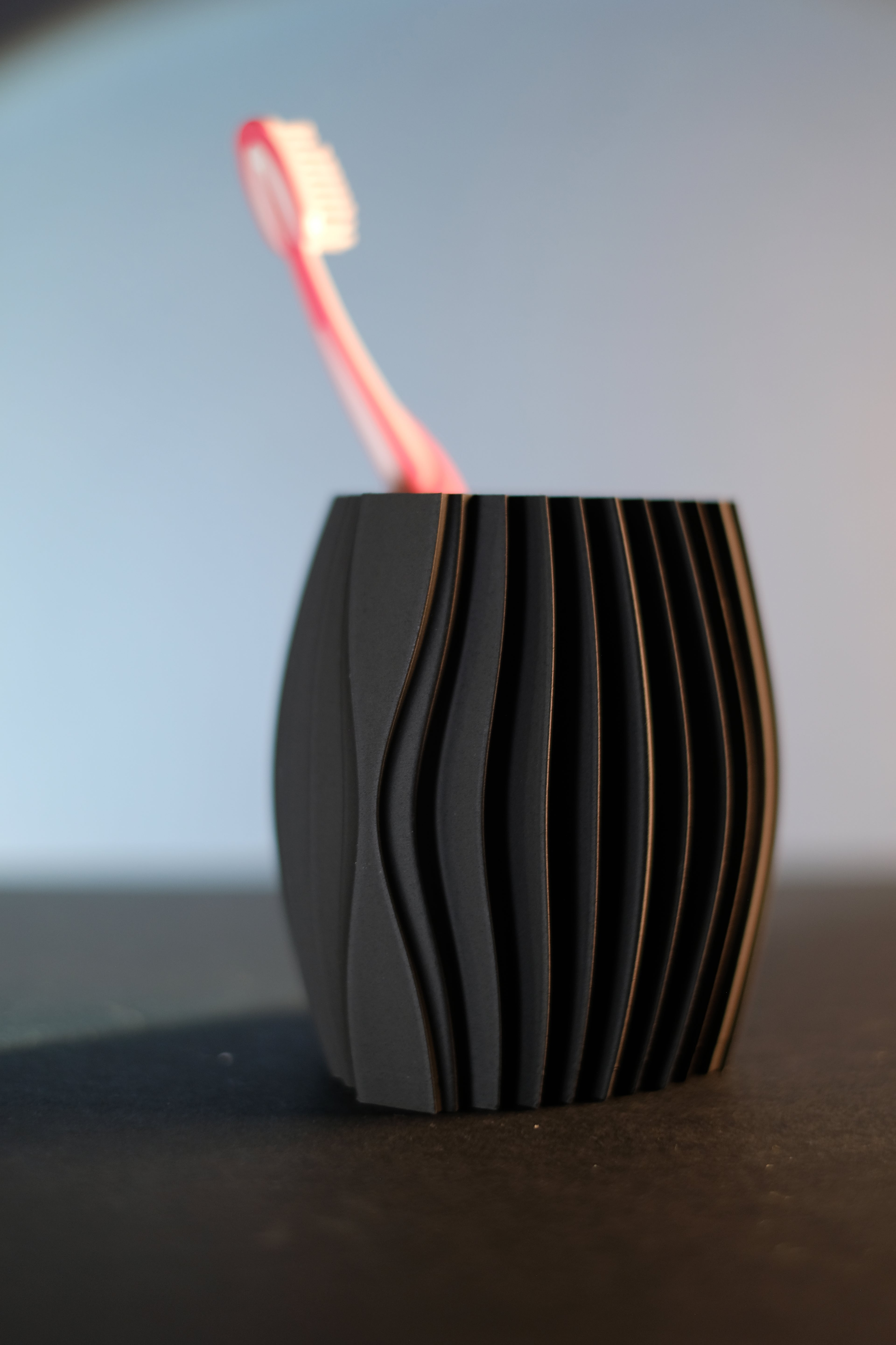 Close front view of the black ripple toothbrush holder with one pink toothbrush