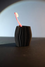 Black sculptural toothbrush holder with wave ribs standing on a dark tabletop