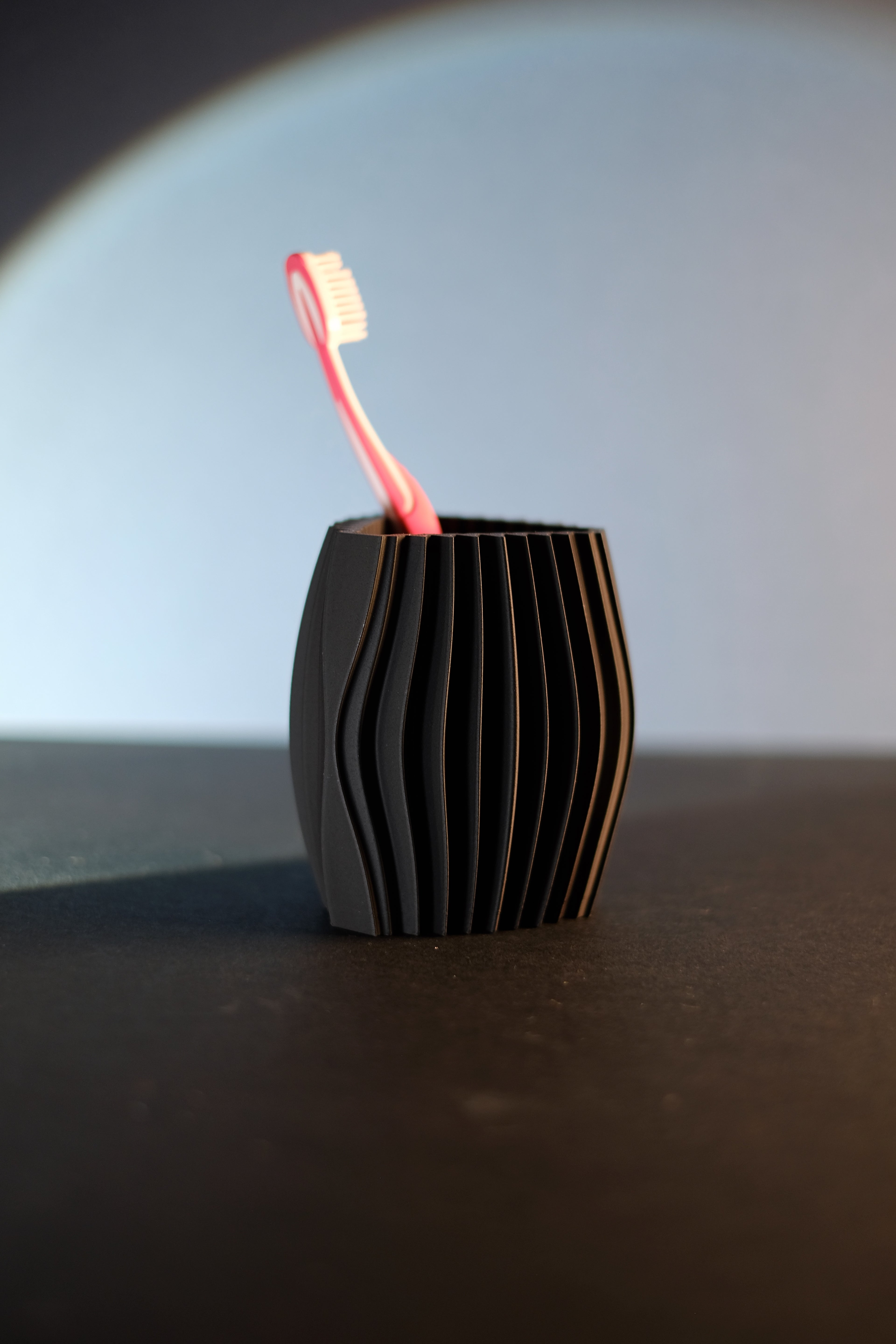 Black sculptural toothbrush holder with wave ribs standing on a dark tabletop