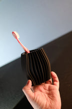 Hand holding the compact black ribbed toothbrush organiser with a pink toothbrush