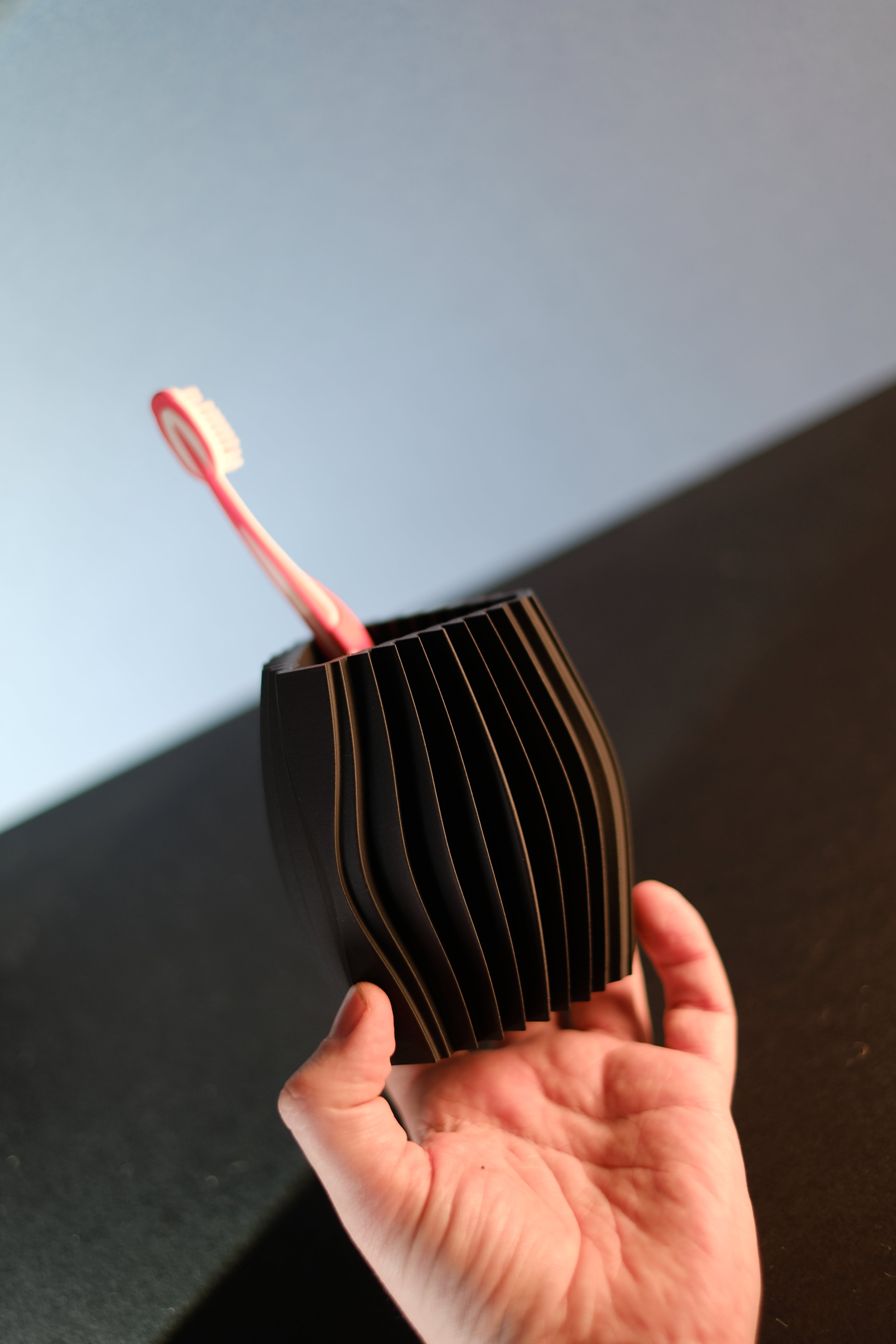 Hand holding the compact black ribbed toothbrush organiser with a pink toothbrush