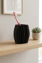 Black wave-textured toothbrush holder displayed on a light wooden bathroom shelf