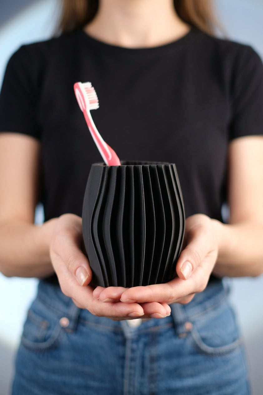 Person holding the black sculptural toothbrush holder to show its compact size