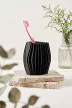 Black ribbed toothbrush holder on stacked stone tiles beside a small glass vase
