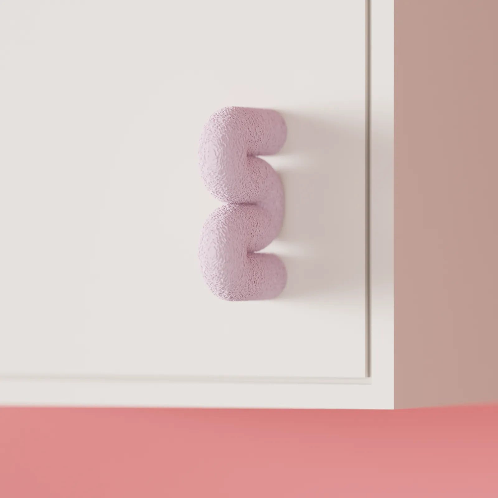 Close front view of the pink Wibble cabinet door handle fitted to a white furniture panel