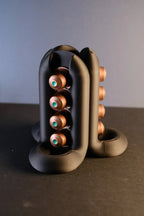 Angled view of the black three-way coffee pod holder showing four capsules along one curved rail