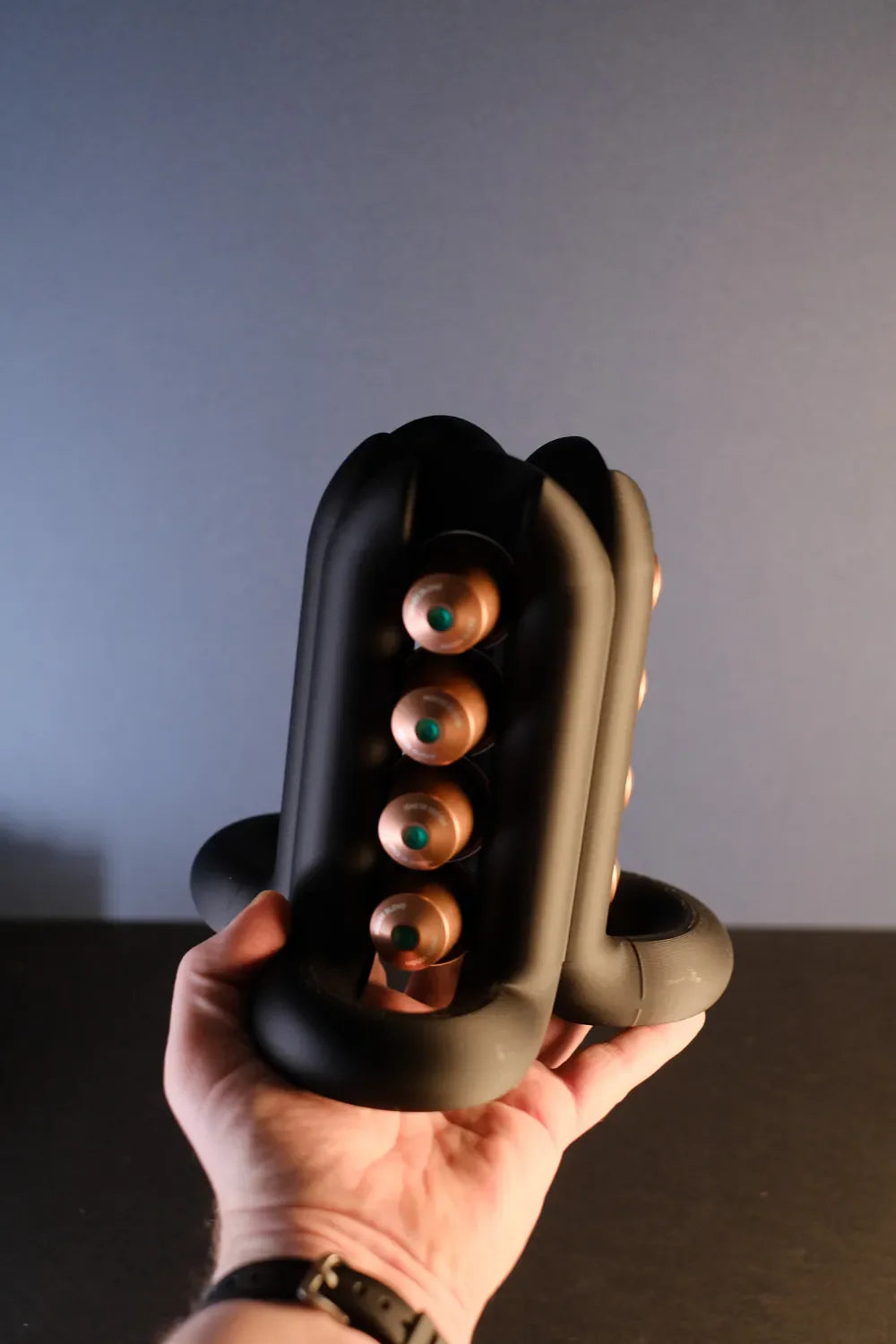 Hand-held close view of the black coffee pod holder showing one four-capsule storage side