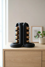 Black three-way coffee pod holder displayed on a light wood cabinet in a bright kitchen setting