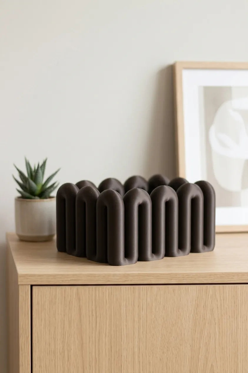 Black sculptural Wibble organiser on a light wood cabinet beside decorative props