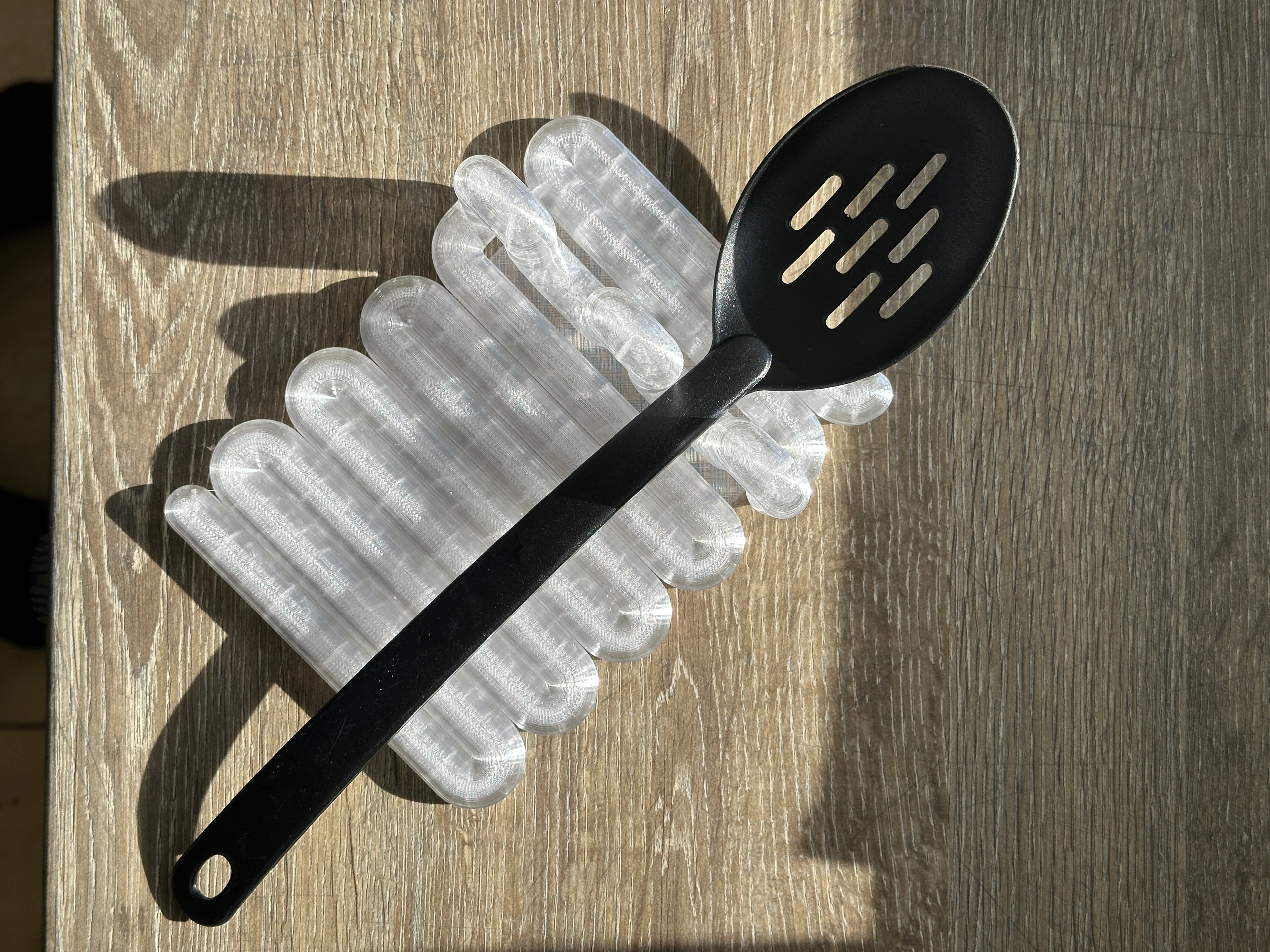 Clear Wibble kitchen utensil rest holding a black slotted spoon in a real product photograph